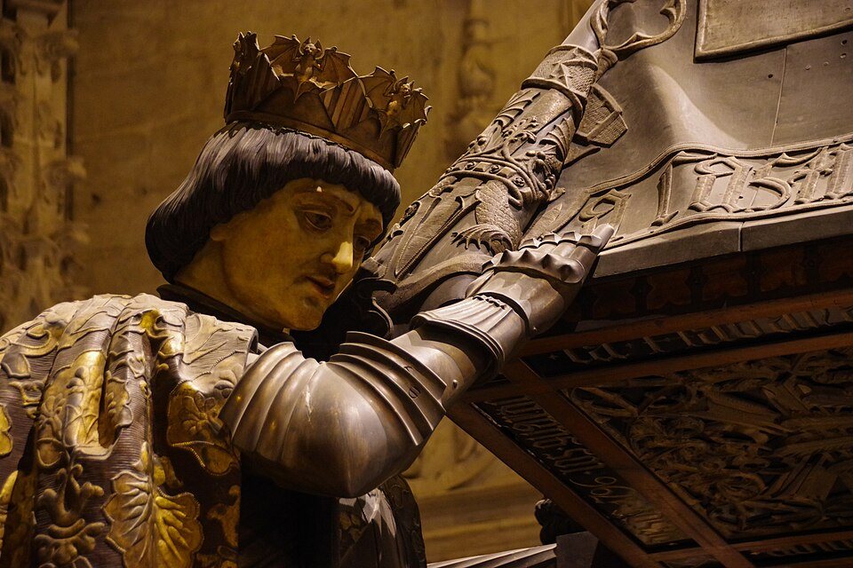 A crowned bronze bearer at the front of Columbus's tomb, supporting the coffin on his shoulder.