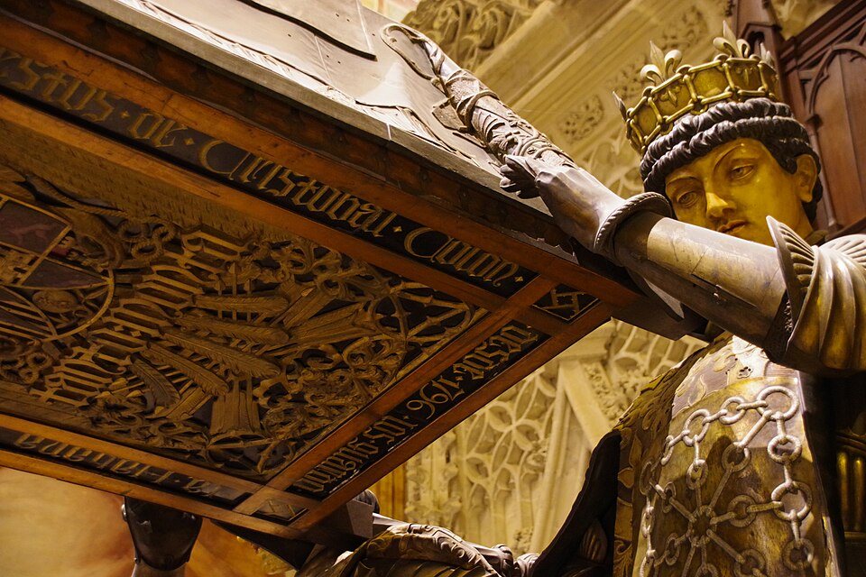 The carved underside of the coffin above a crowned bearer, seen close up.