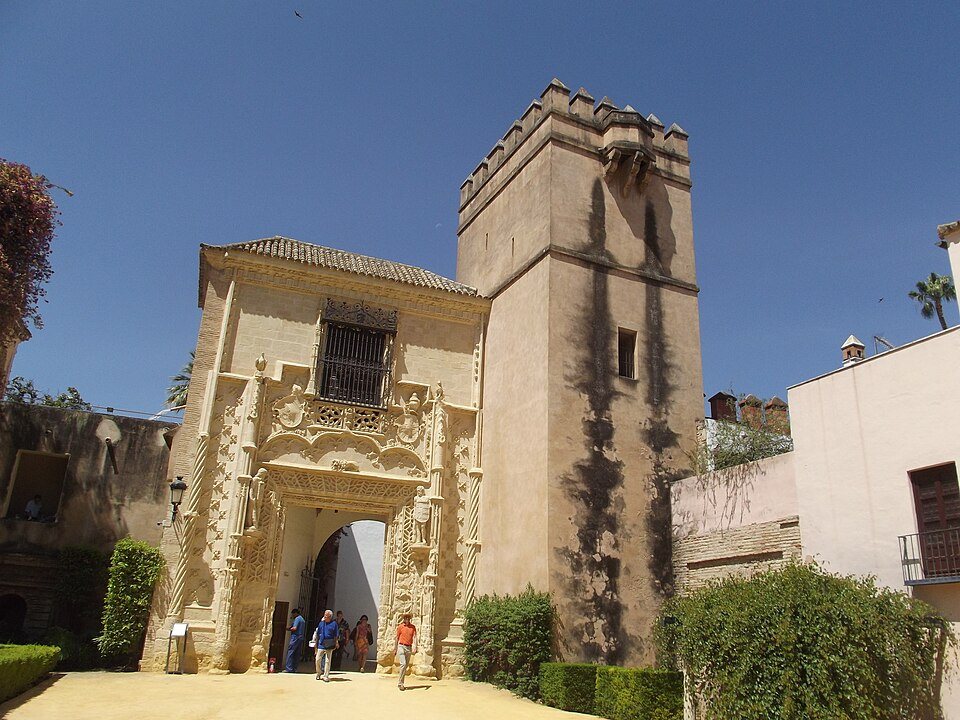 The Marchena Door, a carved Gothic gateway beside a brick tower in the Alcázar gardens.